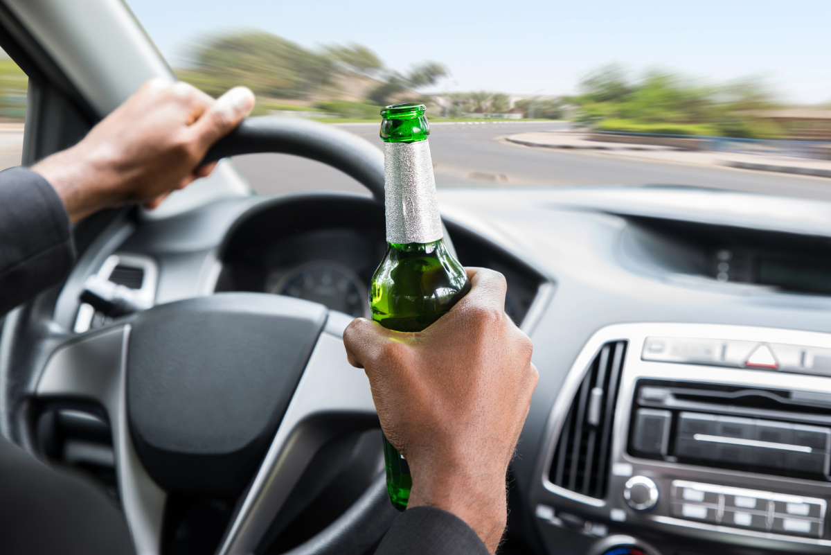 Driver holding an open bottle of beer in one hand while steering with the other